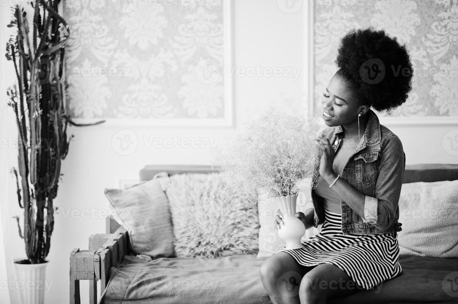 mulher afro-americana atraente com cabelo afro usa saia e jaqueta jeans, posou no quarto branco. modelo preto elegante. foto