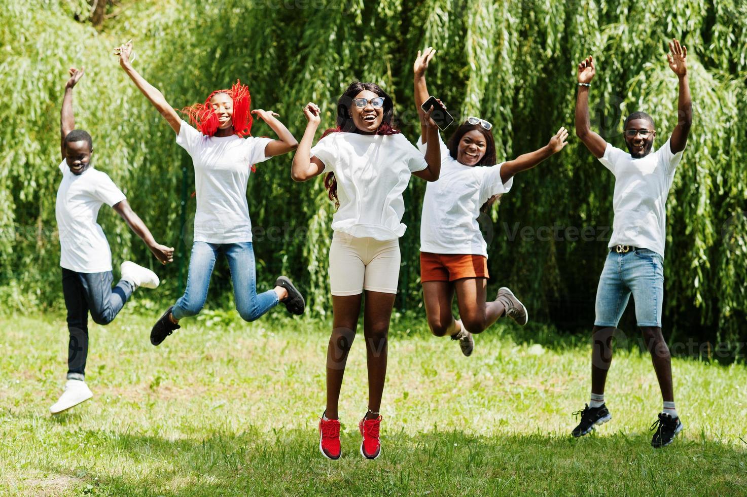 grupo de povos afro-americanos pulando no parque em camisetas brancas. foto