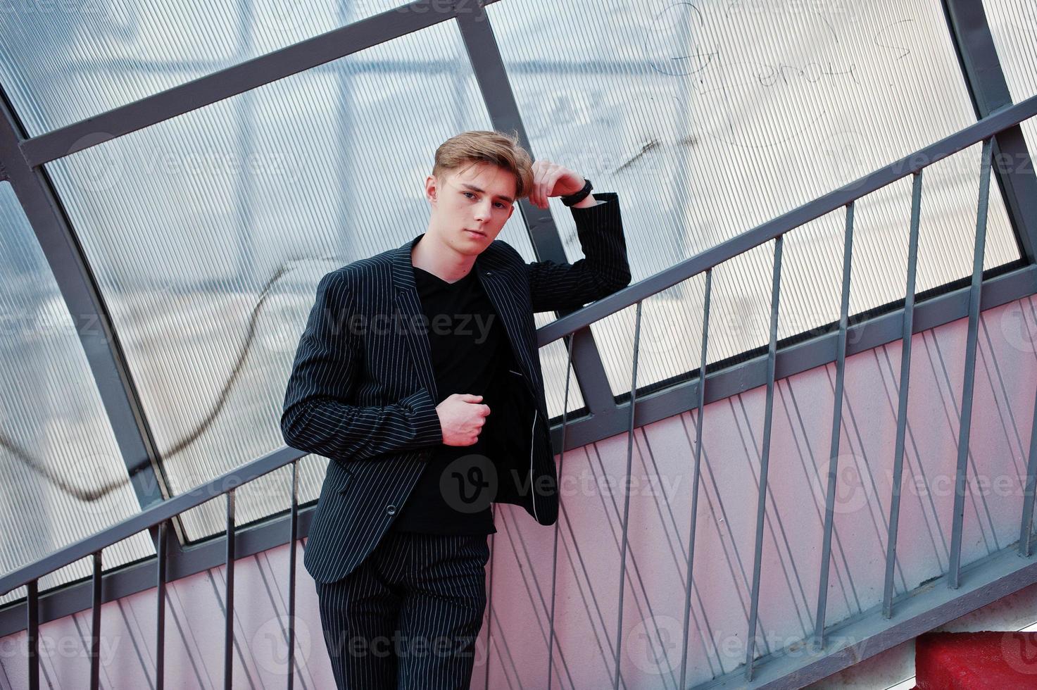 jovem macho macho elegante na jaqueta preta posou ao ar livre da rua. homem modelo incrível no tonel de escadas vermelhas. foto