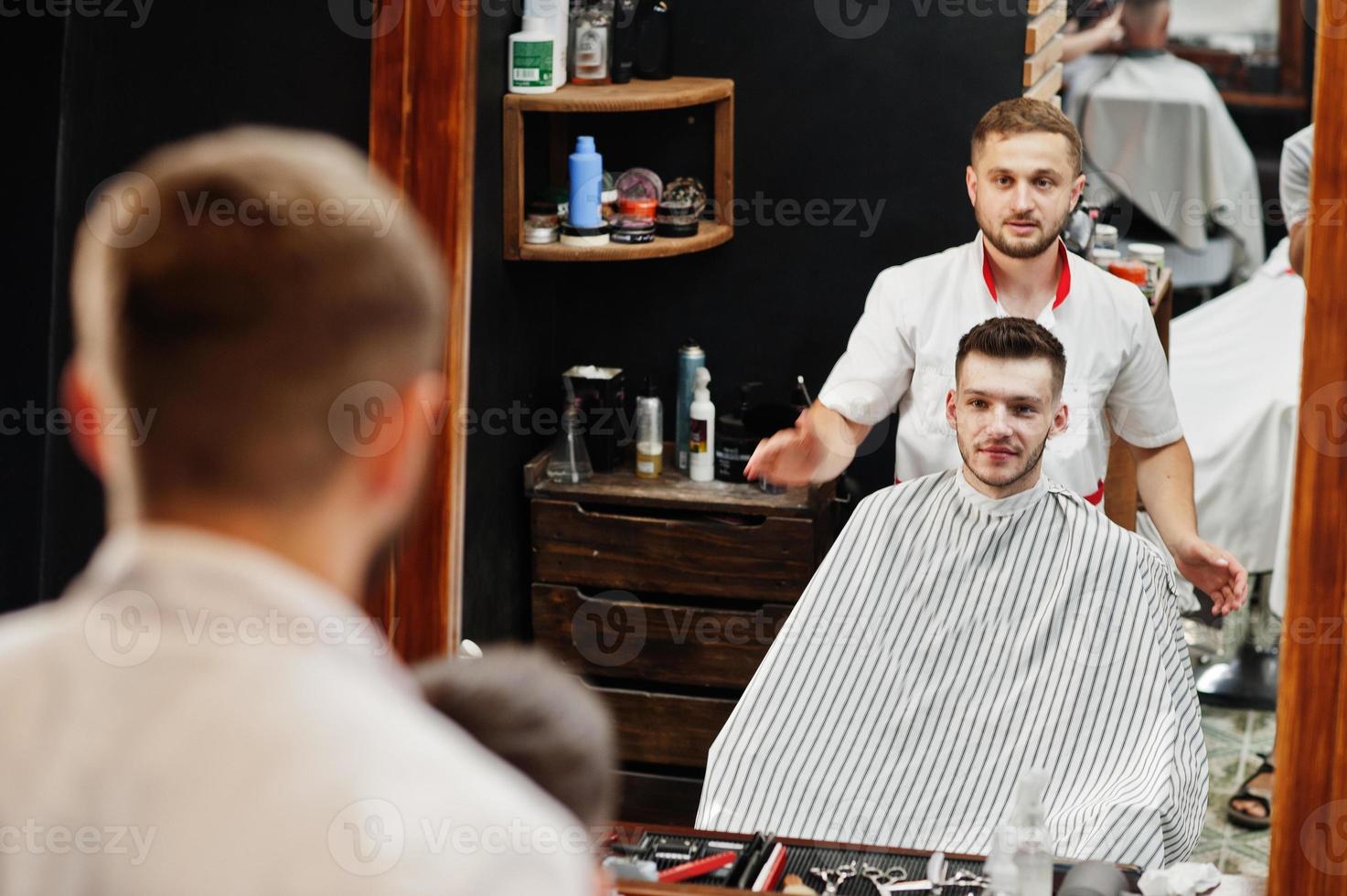 jovem barbudo cortando o cabelo pelo cabeleireiro enquanto está sentado na cadeira na barbearia. alma de barbeiro. foto