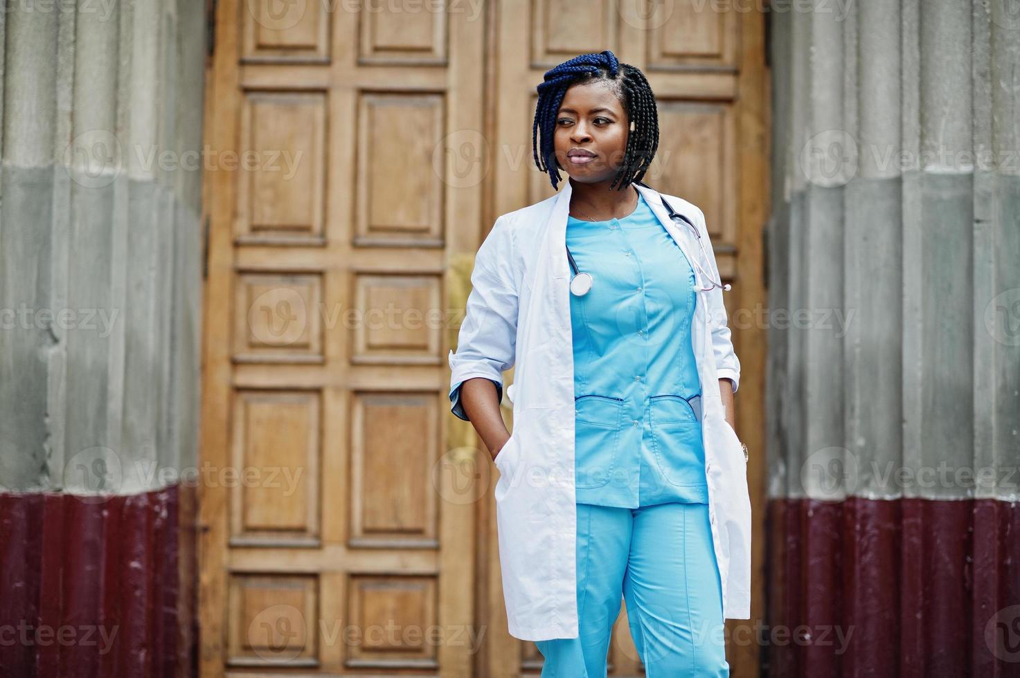 elegante médico americano africano com estetoscópio e jaleco posou contra a porta do hospital. foto