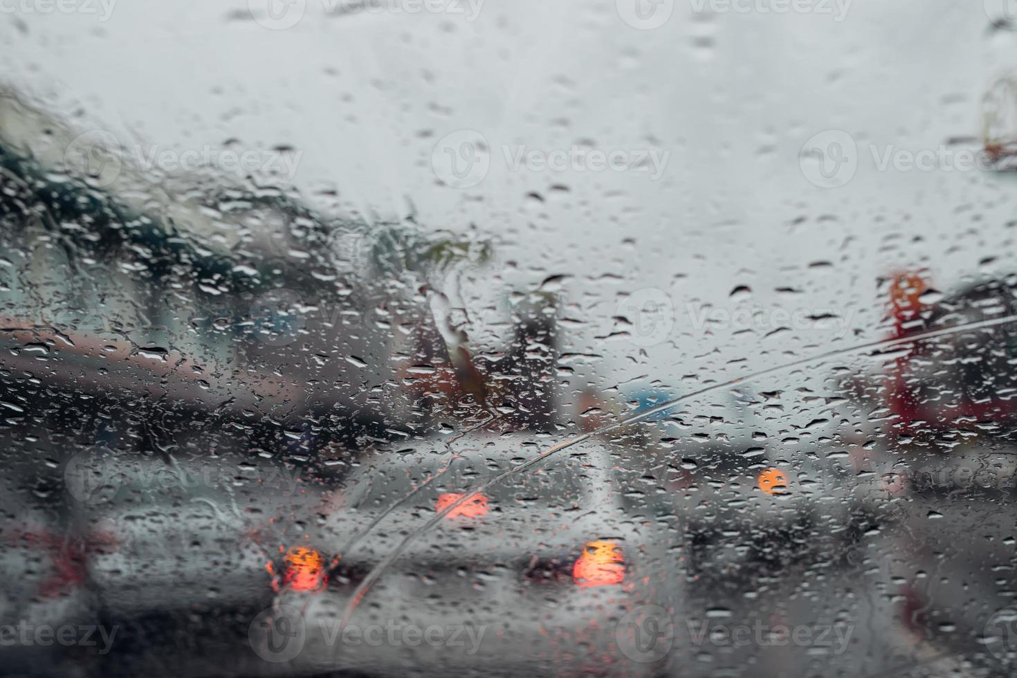 gotas de chuva caem no para-brisa de vidro à noite. rua na chuva forte. luz de cauda bokeh e semáforos na cidade. por favor, dirija o carro com cuidado, estrada escorregadia. foco suave. foto