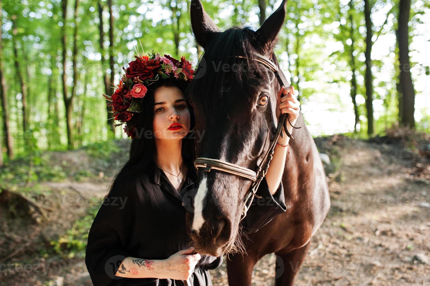 garota mística em grinalda veste em preto com cavalo em madeira. foto