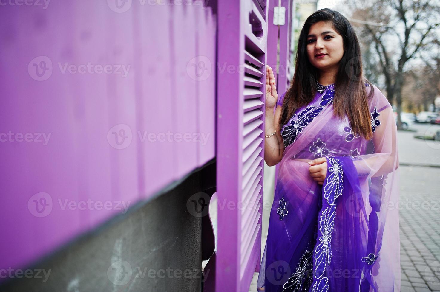 garota hindu indiana no tradicional saree violeta posou na rua contra janelas roxas. foto