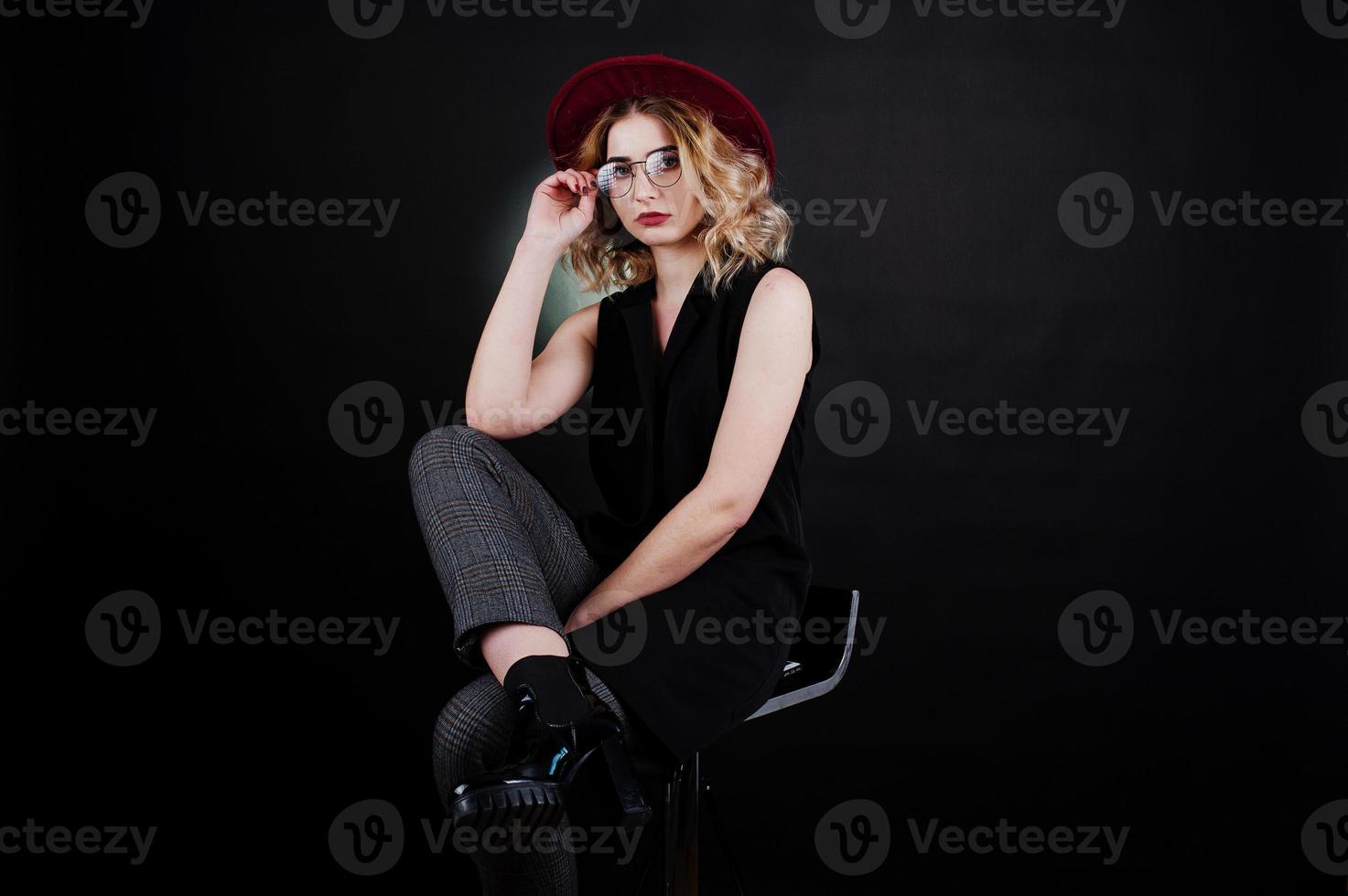 retrato de estúdio de menina loira com roupa preta, chapéu vermelho e óculos contra um fundo escuro. foto