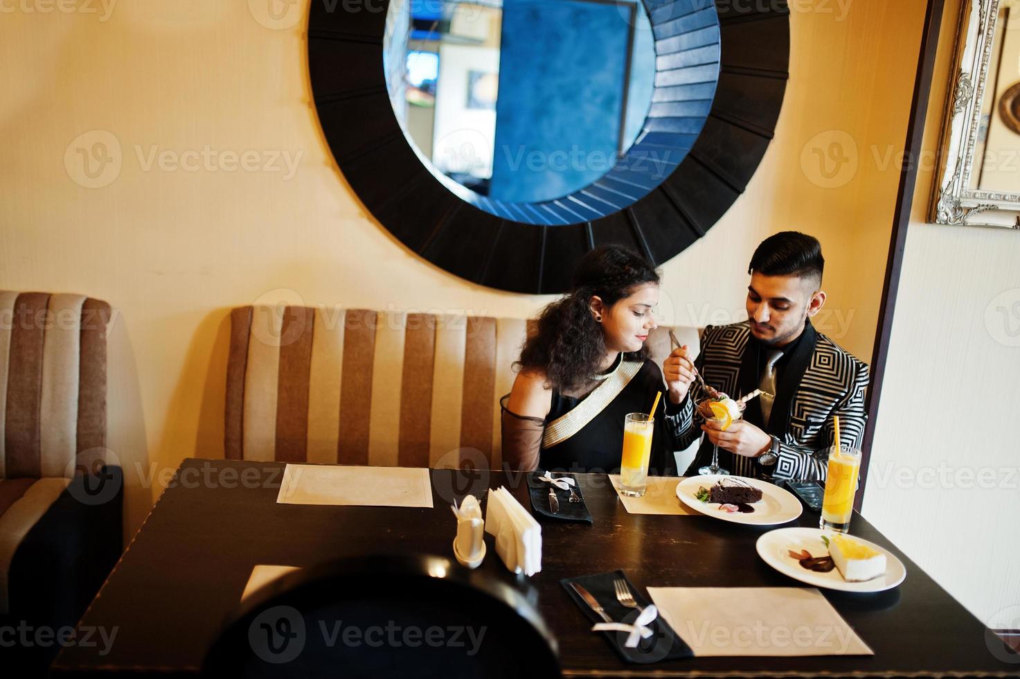 lindo casal indiano apaixonado, veste saree e terno elegante, sentado no restaurante e comendo sorvete juntos. foto