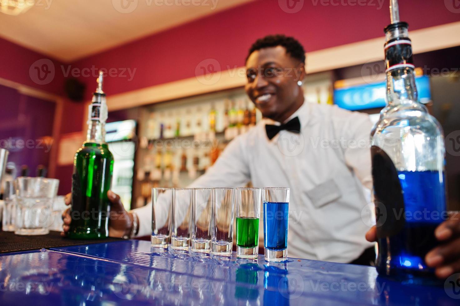 barman americano africano no bar fazendo coquetéis em tiros. preparação de bebidas alcoólicas. foto