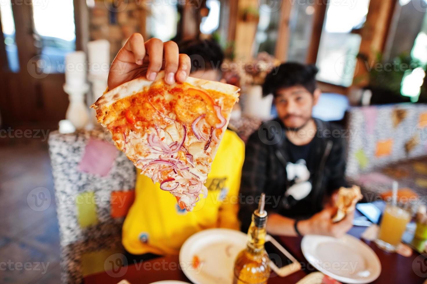 caras amigos asiáticos comendo pizza durante a festa na pizzaria. índios felizes se divertindo juntos, comendo comida italiana e sentados no sofá. foto