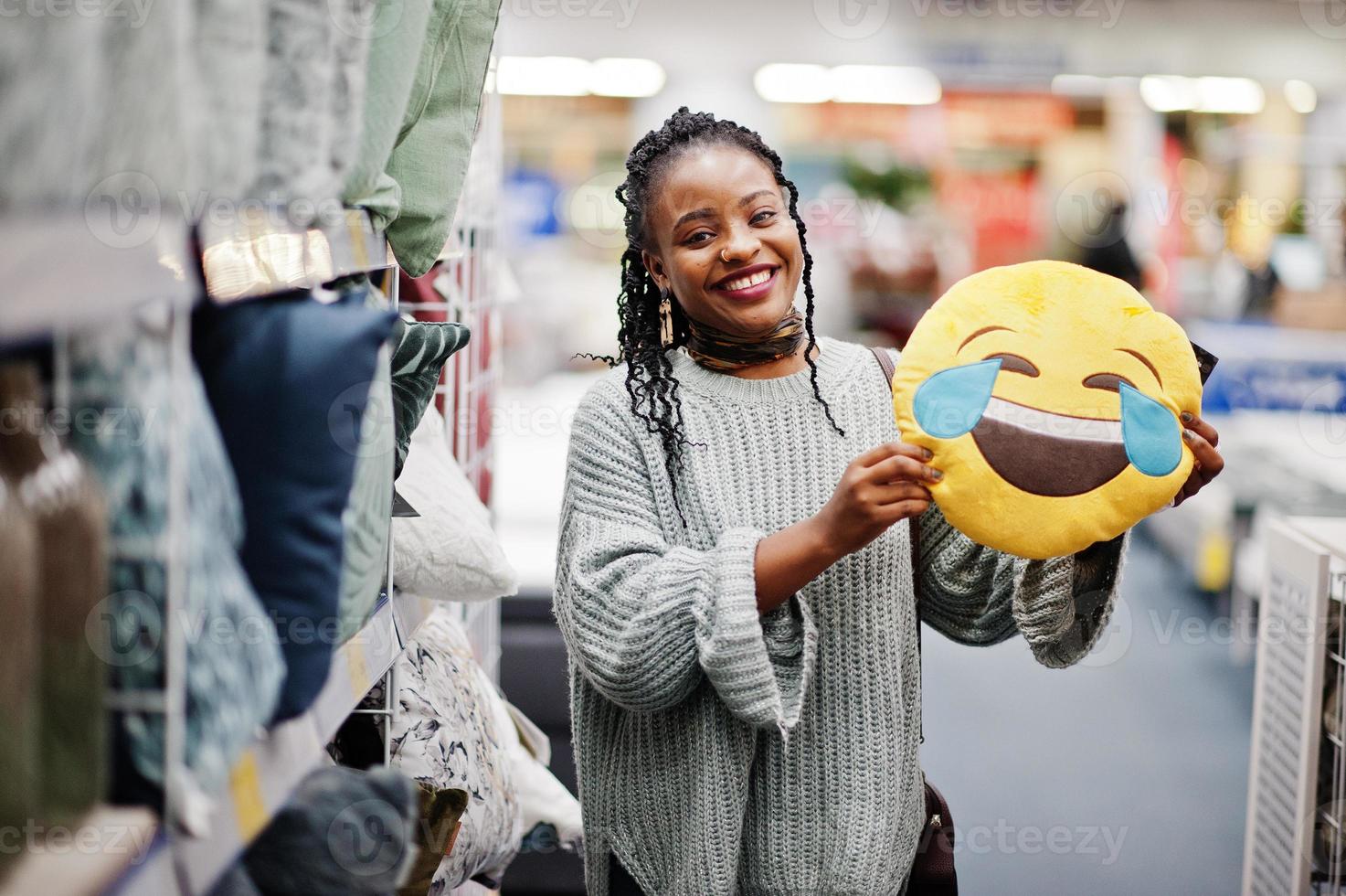 rosto com lágrimas de alegria emoji. lol conceito. mulher africana com travesseiro alto rindo em uma loja de móveis para casa moderna. foto