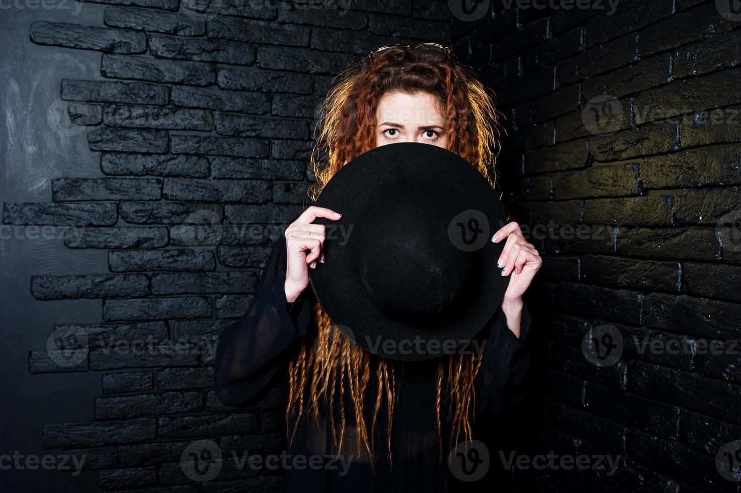 sessão de estúdio de garota de preto com dreads e chapéu em fundo de tijolo. foto