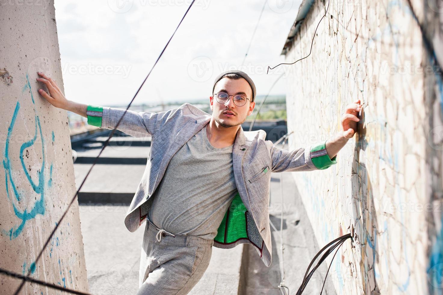 sonhador elegante macho de terno cinza, chapéu e óculos posou no telhado. foto