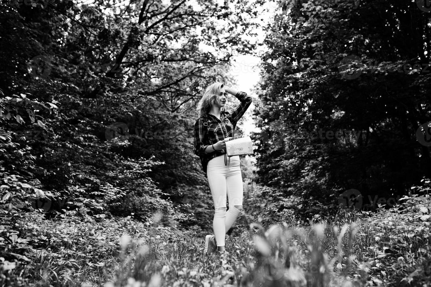 retrato de uma jovem linda loira de camisa xadrez segurando um mapa na floresta. foto