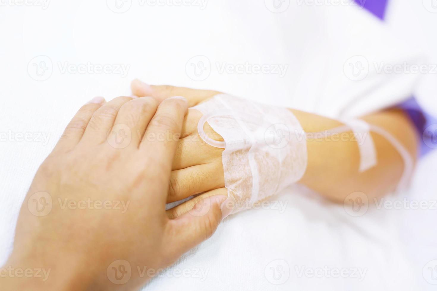 close-up foco no aperto de mão de um paciente doente incentiva o encorajamento na cama na enfermaria do hospital. foto