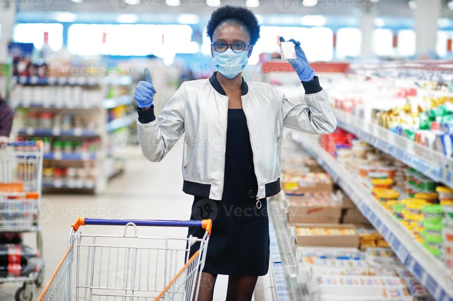 mulher africana usando máscara médica descartável e luvas fazendo compras no supermercado durante o surto de pandemia de coronavírus. tempo epidêmico. foto