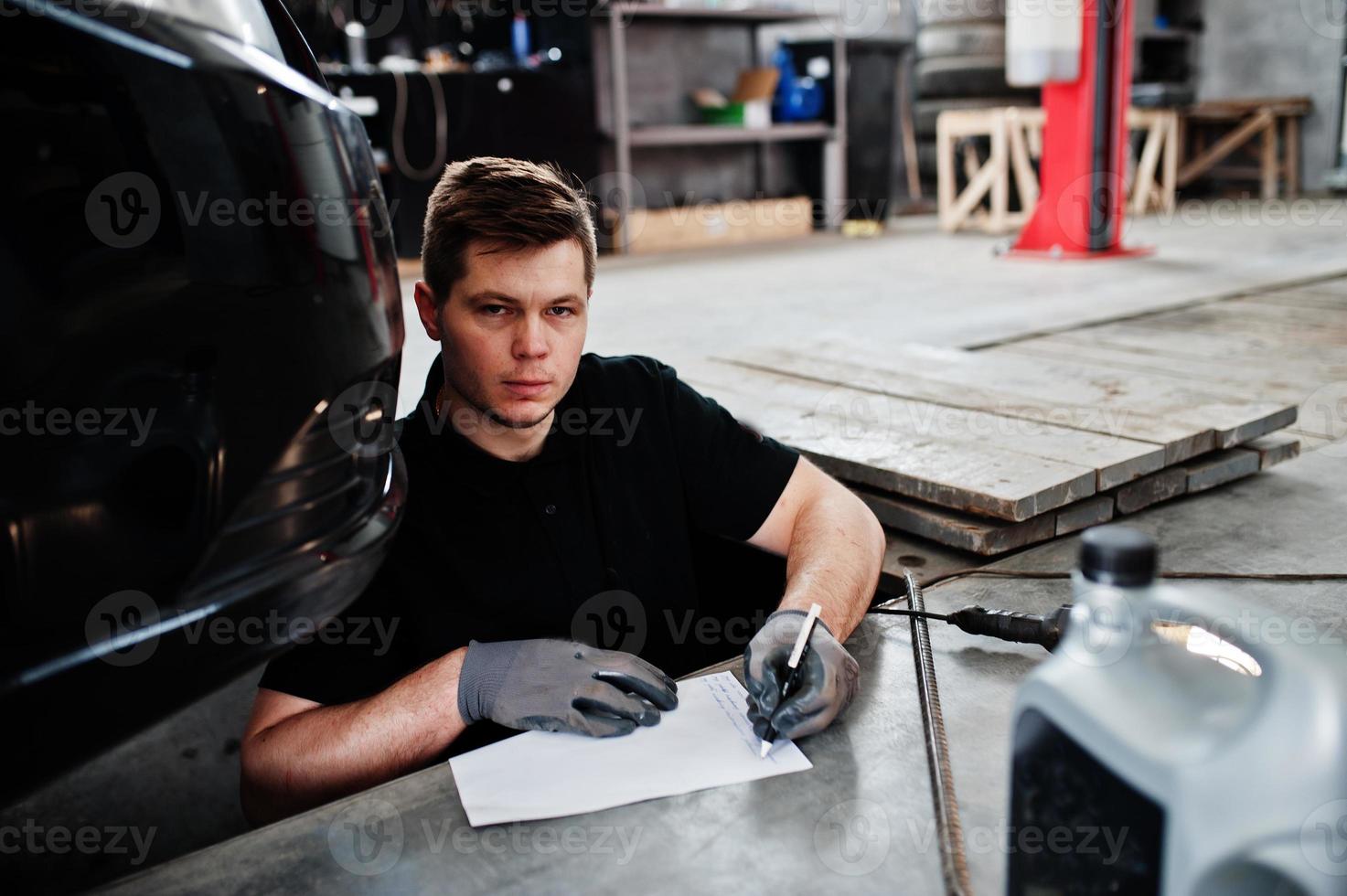 tema de reparação e manutenção de automóveis. mecânico de uniforme trabalhando em auto serviço, escrever por caneta conclusão. foto