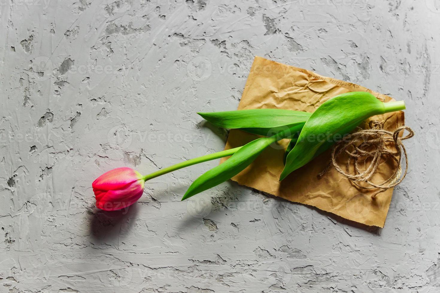 vista superior da tulipa vermelha florescendo fresca em papel ofício e plano de fundo texturizado cinza. espaço de cópia foto