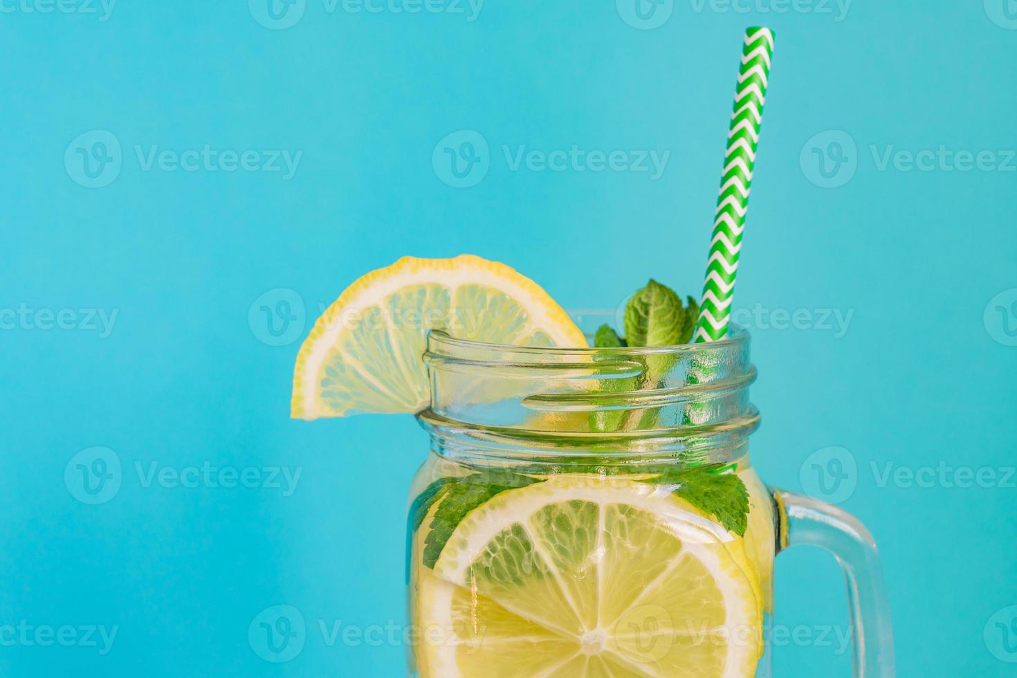 vidro de jarra de limonada caseira com limões, hortelã e palha de papel em fundo turquesa. bebida refrescante de verão. foto