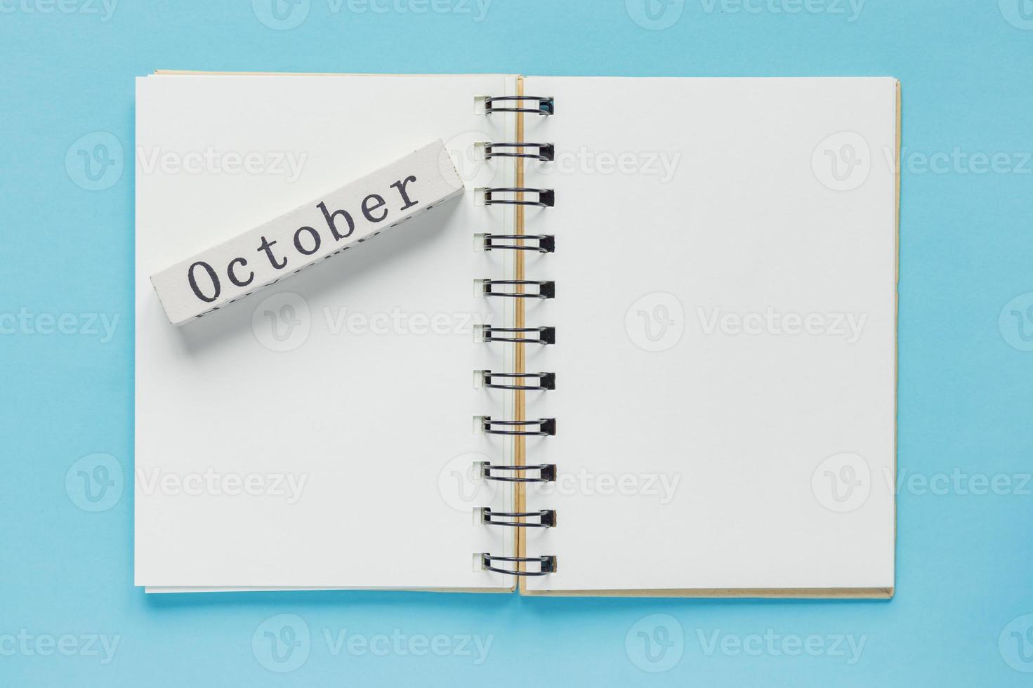 caderno espiral limpo para notas e mensagens e barra de calendário de madeira de outubro sobre fundo azul. postura plana de negócios mínima foto