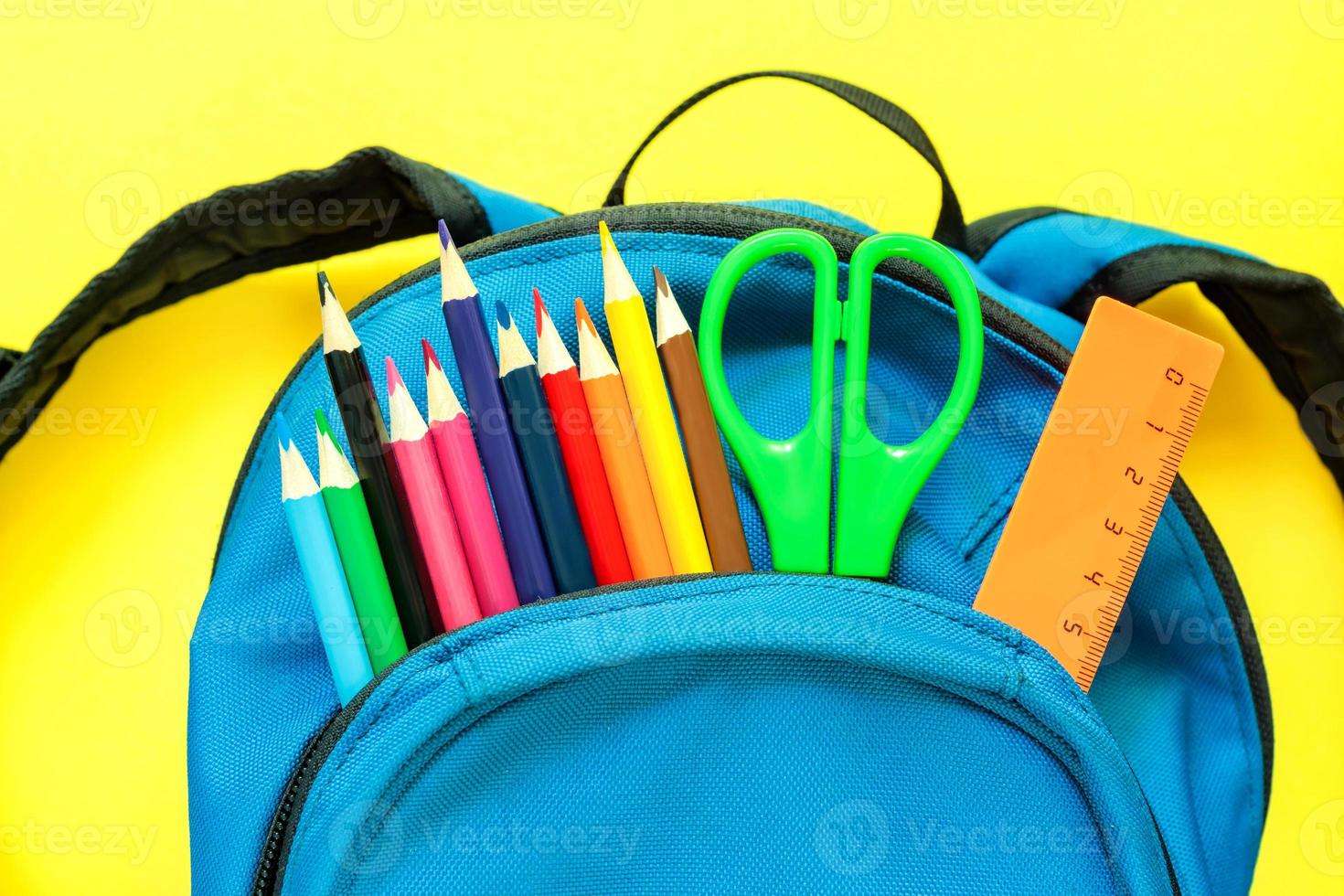 mochila azul com artigos de papelaria coloridos diferentes sobre fundo amarelo. de volta à escola foto