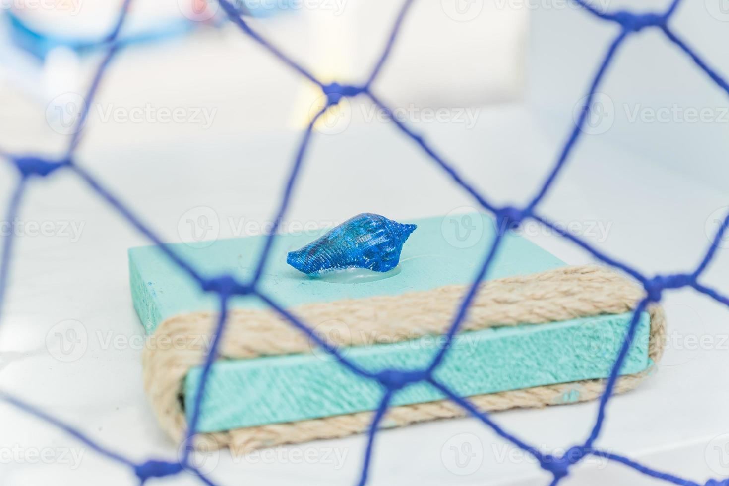 lembrança do mar. concha pintada de azul na prateleira atrás da rede de pesca foto