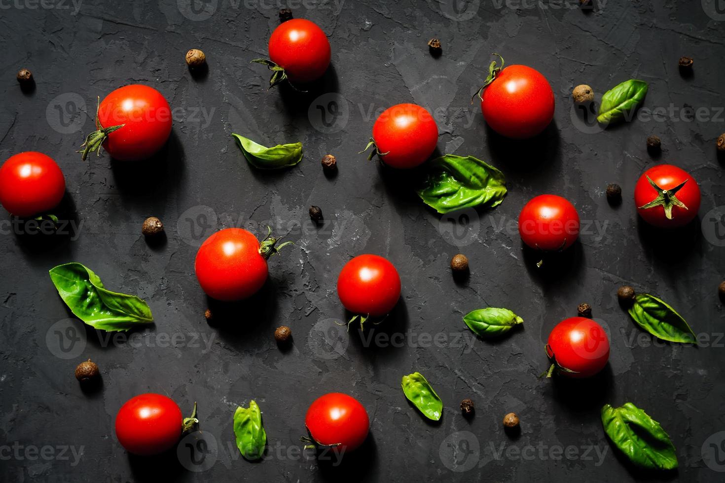 tomate cereja fresco com folhas de manjericão e pimenta preta em uma mesa de pedra preta, padrão vegetal, vista superior foto