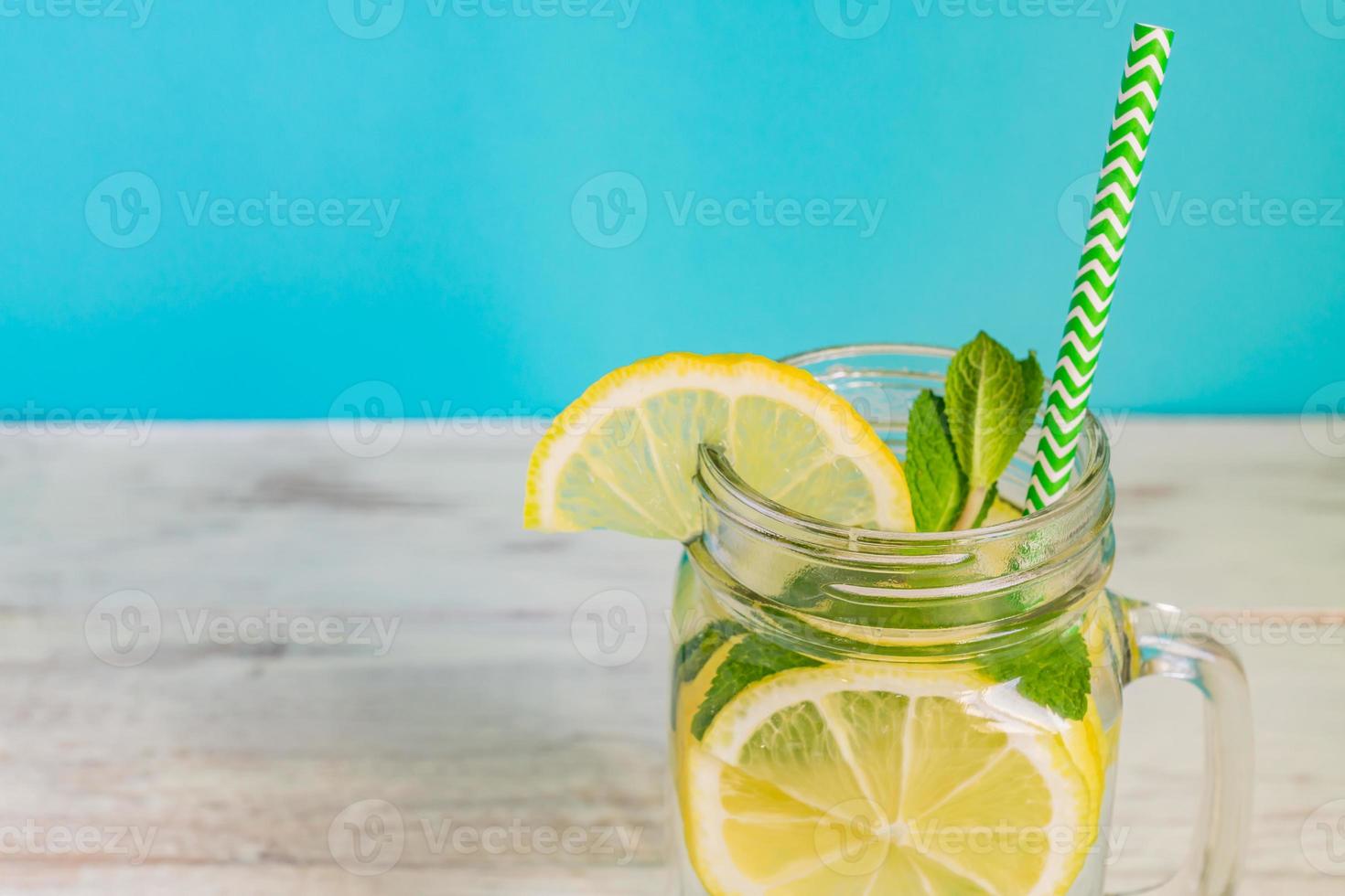 vidro de jarra de limonada caseira com limões, hortelã e palha de papel em fundo turquesa. bebida refrescante de verão. foto