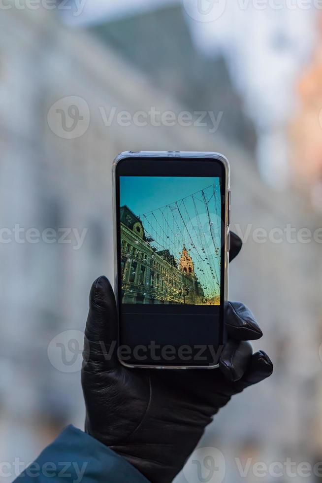 mulher mão uma luva de couro preto segurando smartphone preto para tirar foto da cidade natal em um dia ensolarado