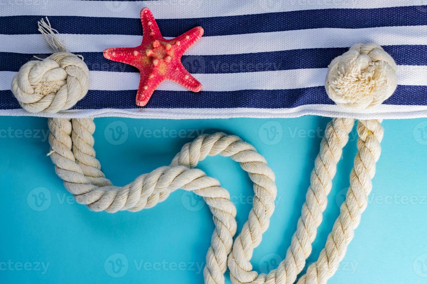 conchas do mar, estrela do mar e bolsa da marinha com listras têxteis com nós de corda sobre fundo azul claro. férias de verão e conceito de férias foto