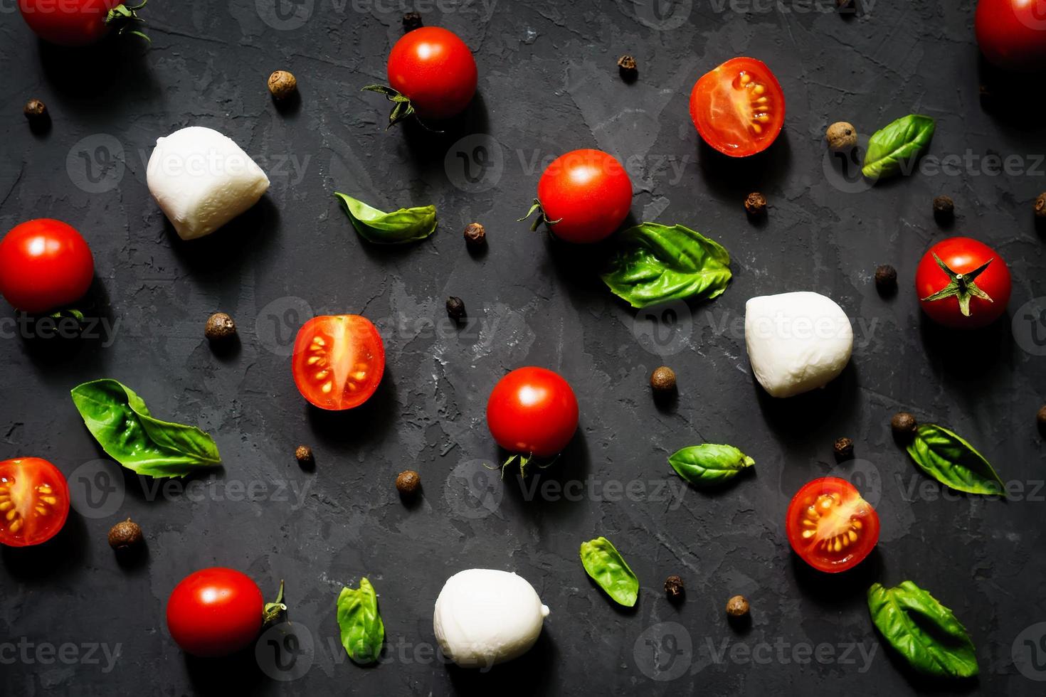 bolas de queijo mussarela com folhas de manjericão fresco e tomate cereja, ingredientes para salada caprese italiana, em um fundo preto. padrão de alimentação foto