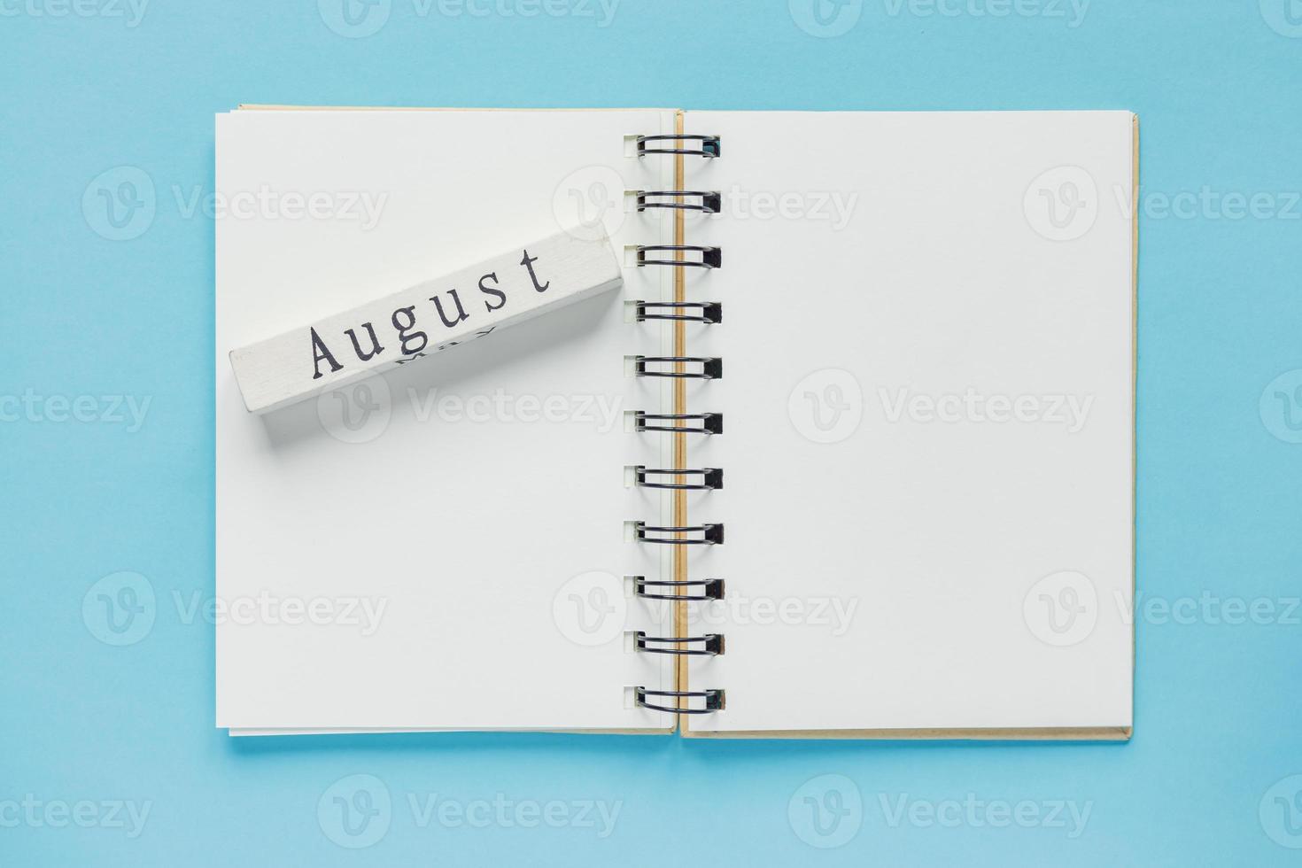 caderno espiral limpo para notas e mensagens e barra de calendário de madeira de agosto sobre fundo azul. postura plana de negócios mínima foto