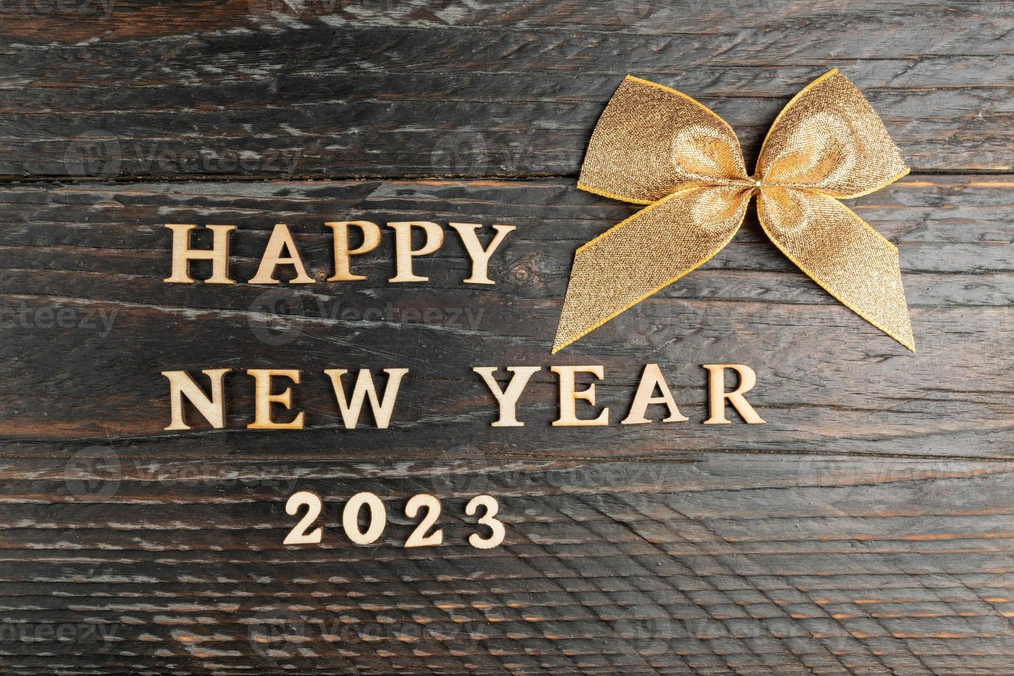 feliz ano novo cartão festivo. fita de ouro amarrada em um arco e texto de madeira feliz ano novo 2023 na mesa de madeira festiva. foto