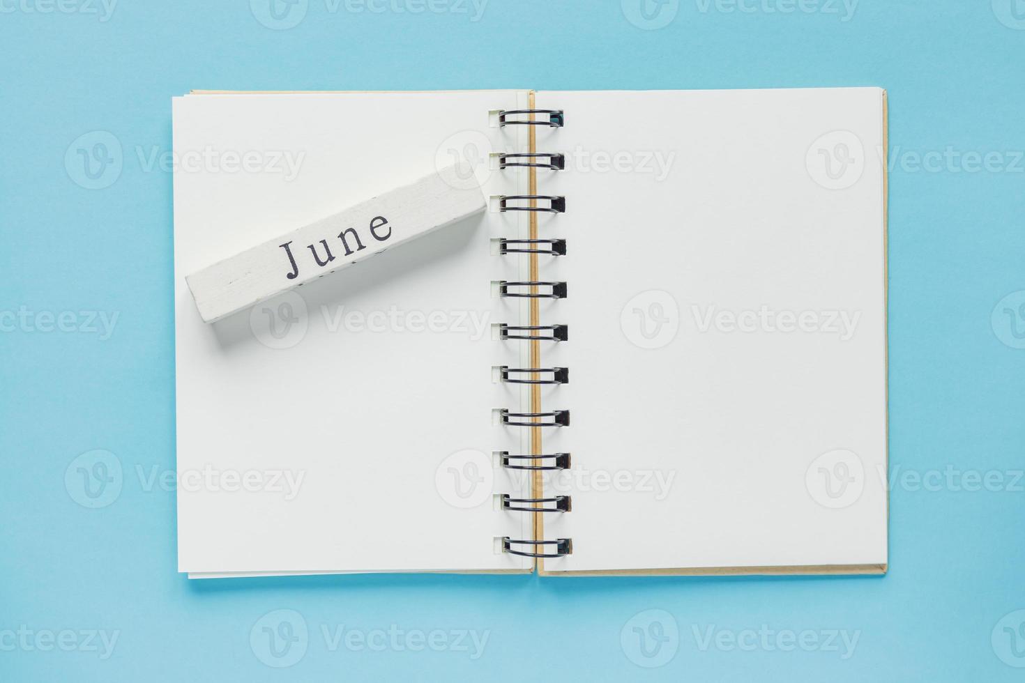 caderno espiral limpo para notas e mensagens e barra de calendário de madeira de junho sobre fundo azul. postura plana de negócios mínima foto