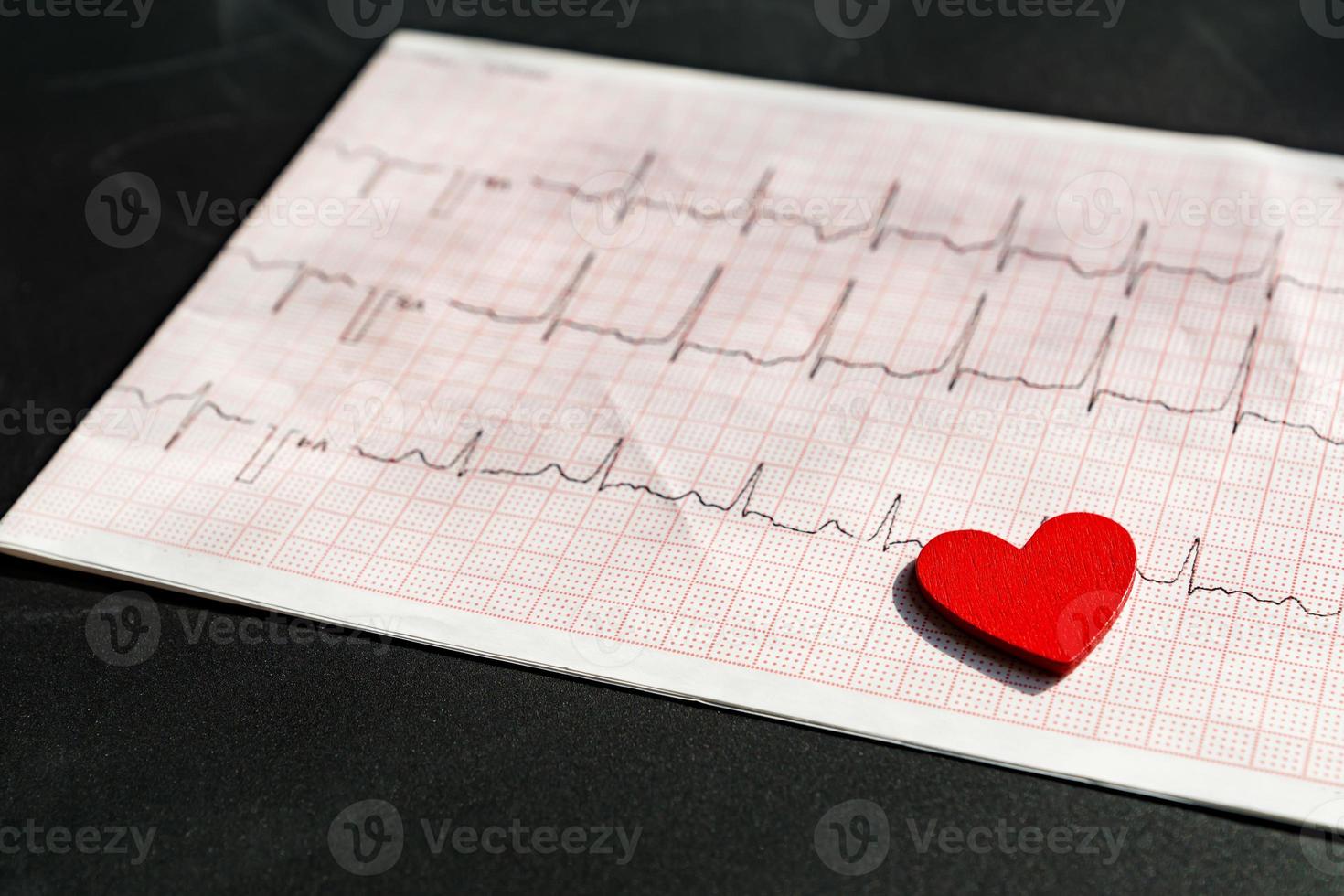 close-up de um eletrocardiograma em papel com coração de madeira vermelho. papel ecg ou ekg em fundo preto. conceito médico e de saúde. foto