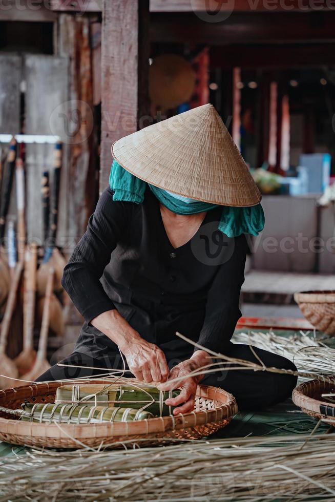 foco mulher velha com vestido tradicional vietnamita ao ba ba fazendo, embrulhando bolo de tet, a comida de tet de ano novo lunar vietnamita ao ar livre pelas mãos. foto