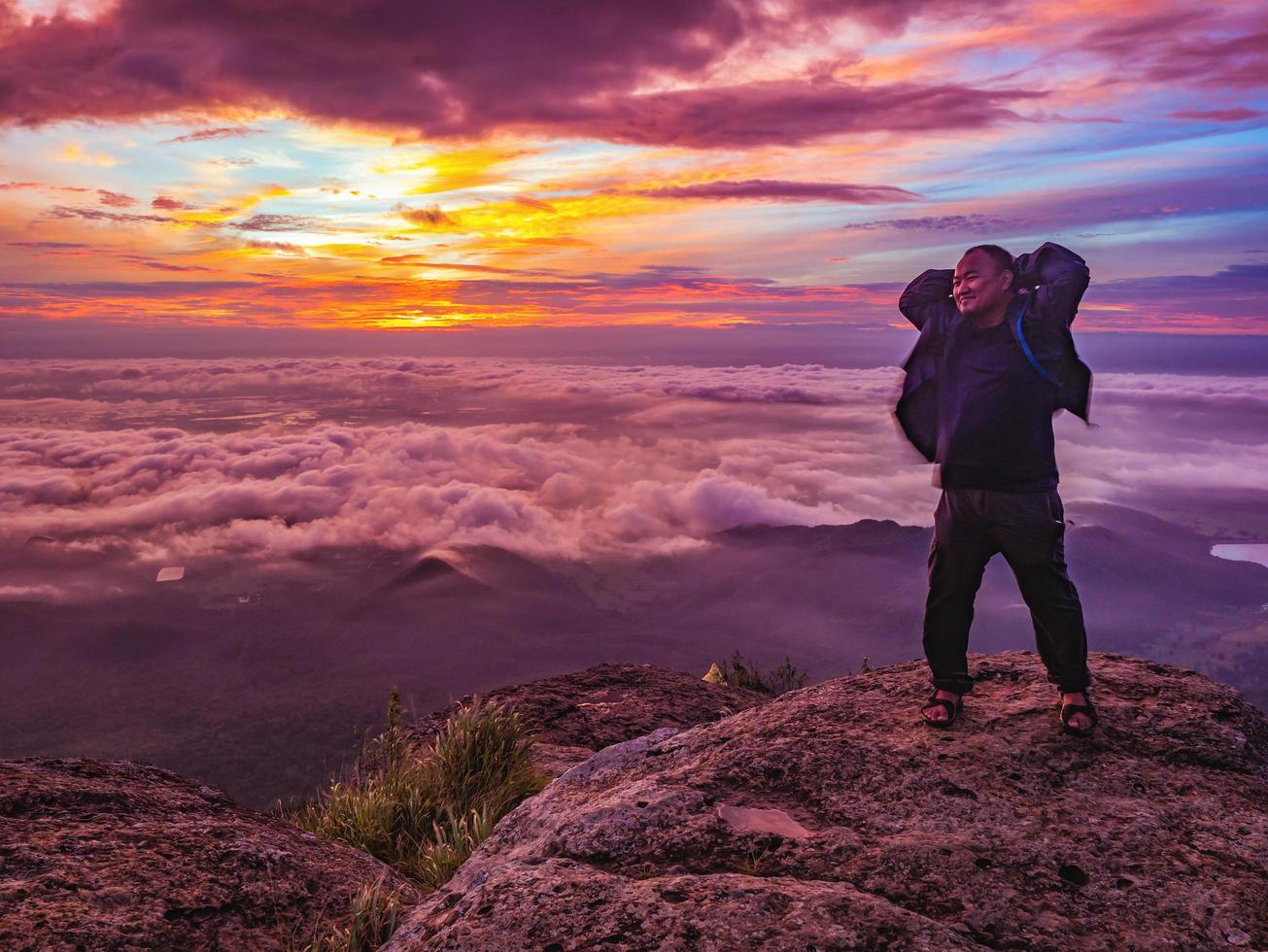 viajante fica em rochoso cilff com céu sunsire e belo mar de nuvens no parque nacional pa na rai khao luang mountian ramkhamhaeng, província de sukhothai, tailândia foto