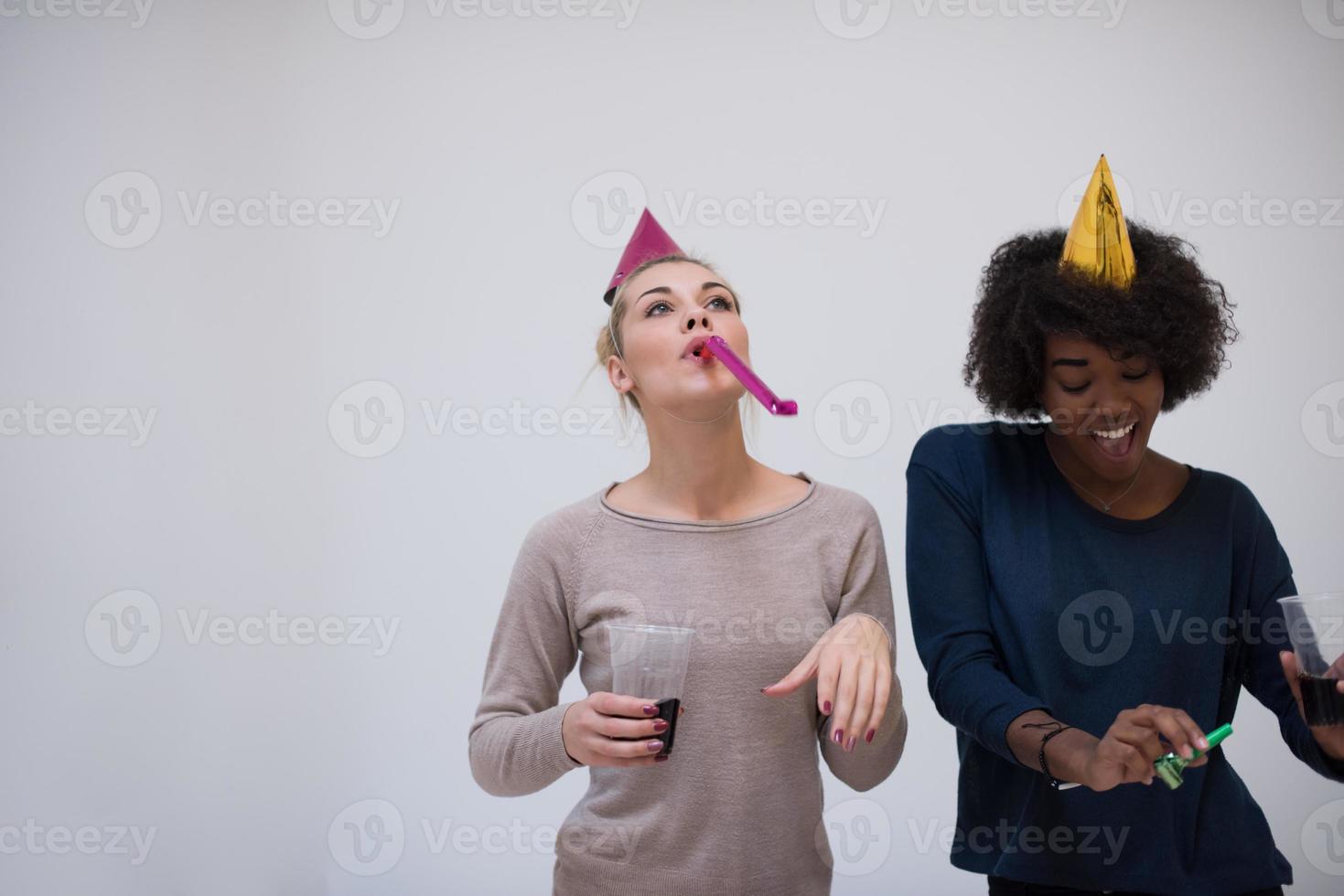 mulheres sorridentes em bonés de festa soprando apitos foto