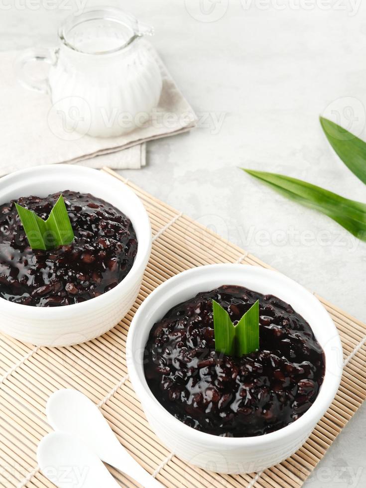 bubur ketan hitam, sobremesa indonésia. mingau de arroz glutinoso preto com leite de coco, açúcar e folha de pandan. servido em uma tigela branca em uma mesa de madeira. foto