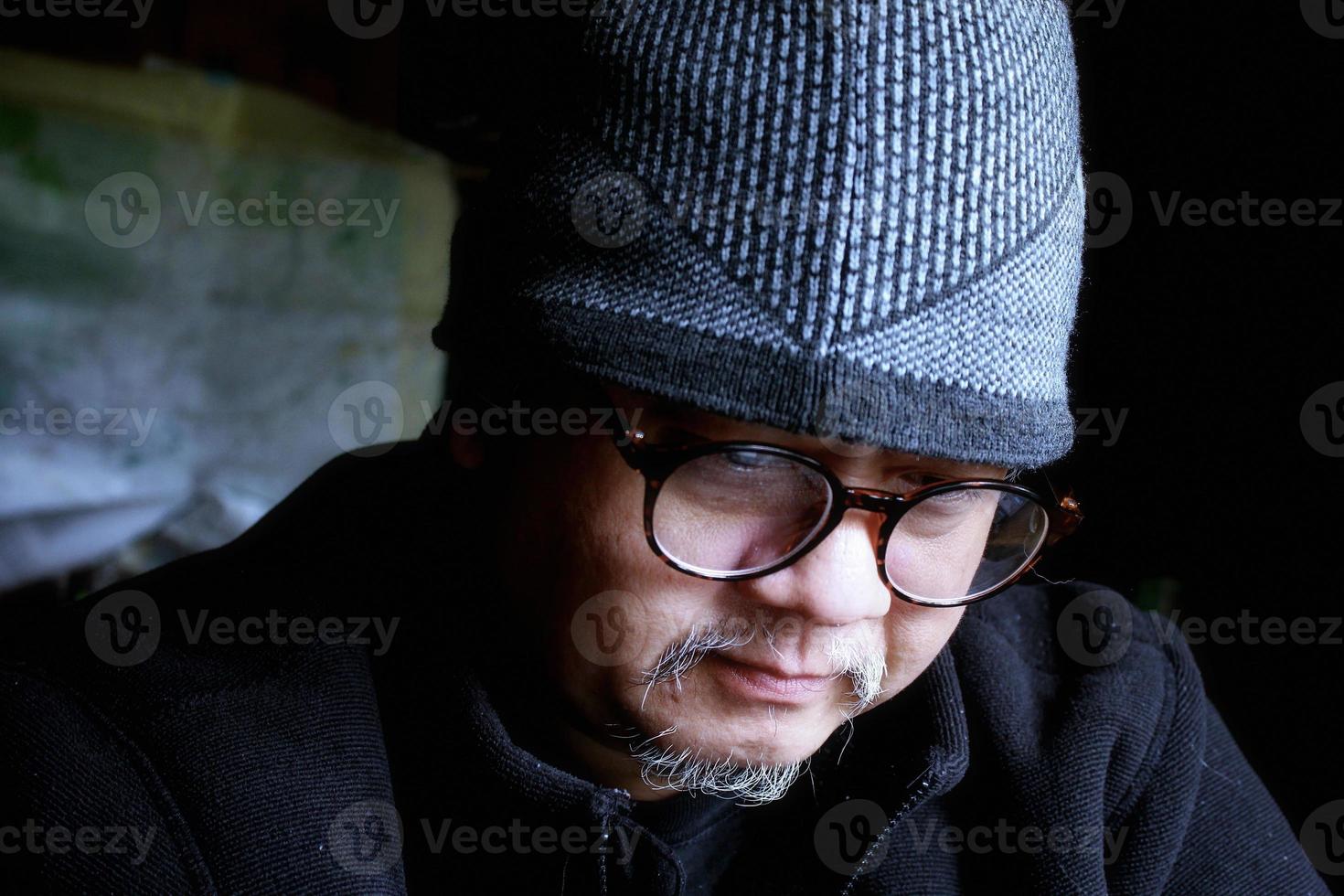 homem asiático barbudo de jaqueta preta e chapéu de malha. trabalhando em um quarto escuro e indo para o trabalho foto