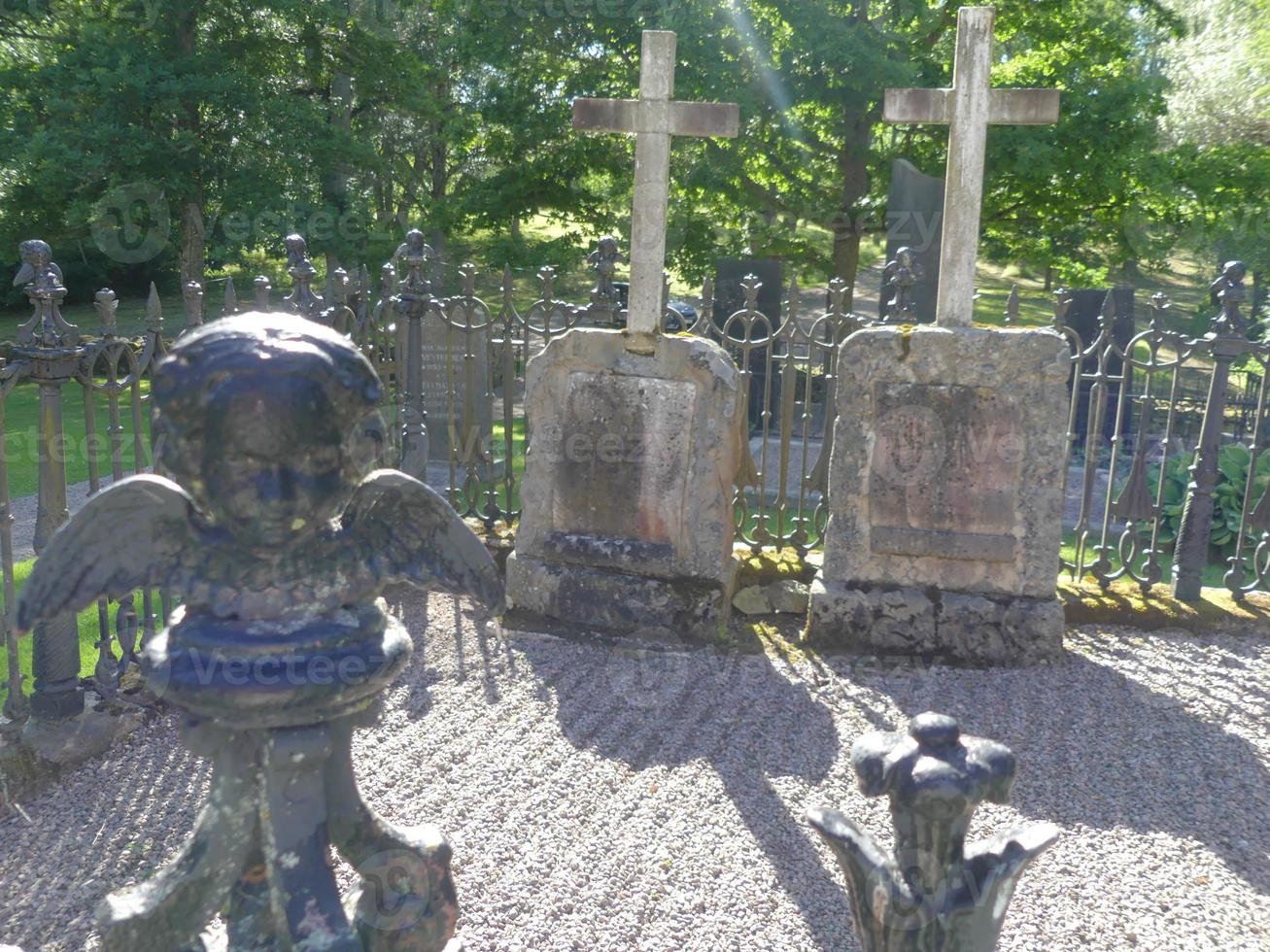 estátua de anjo misteriosa com asas na frente de duas sepulturas com pedras e cruzes no cemitério assustador foto