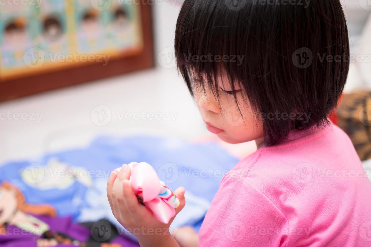 criança asiática fez uma cara triste, olhando para o grampo de cabelo danificado em sua mão. uma menina de 4 anos vestindo uma camisa rosa. foto