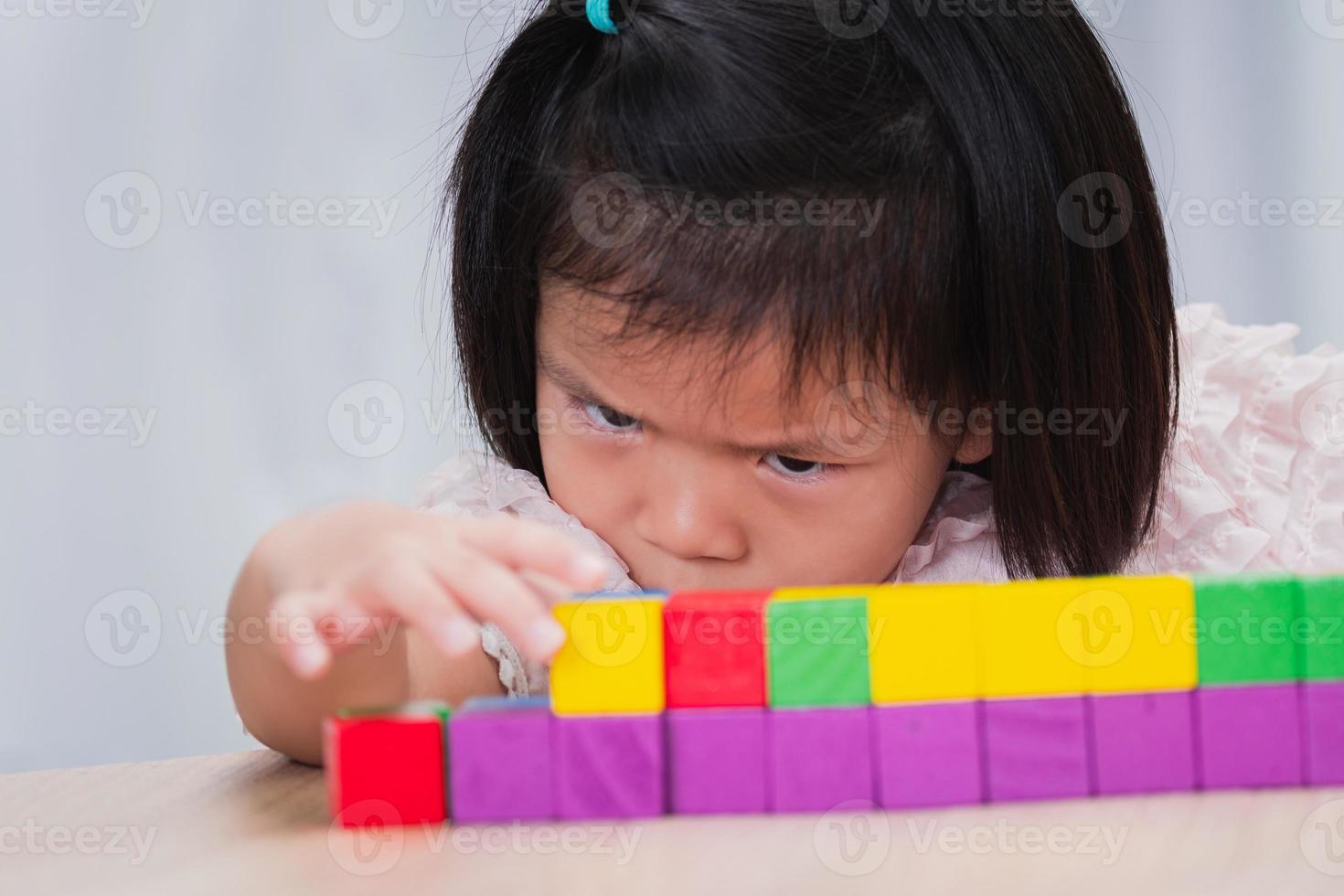 criança menina jogando brinquedos de madeira em casa ou escola de jardim de infância. criança está seriamente classificando e construindo os blocos de madeira, ela aponta os blocos de brinquedo para combinar. conceito de crianças perfeccionistas. foto