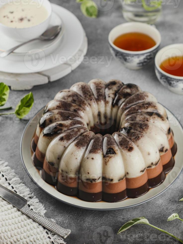 bolo de pudim de chocolate servido em um prato com um copo de chá quente foto