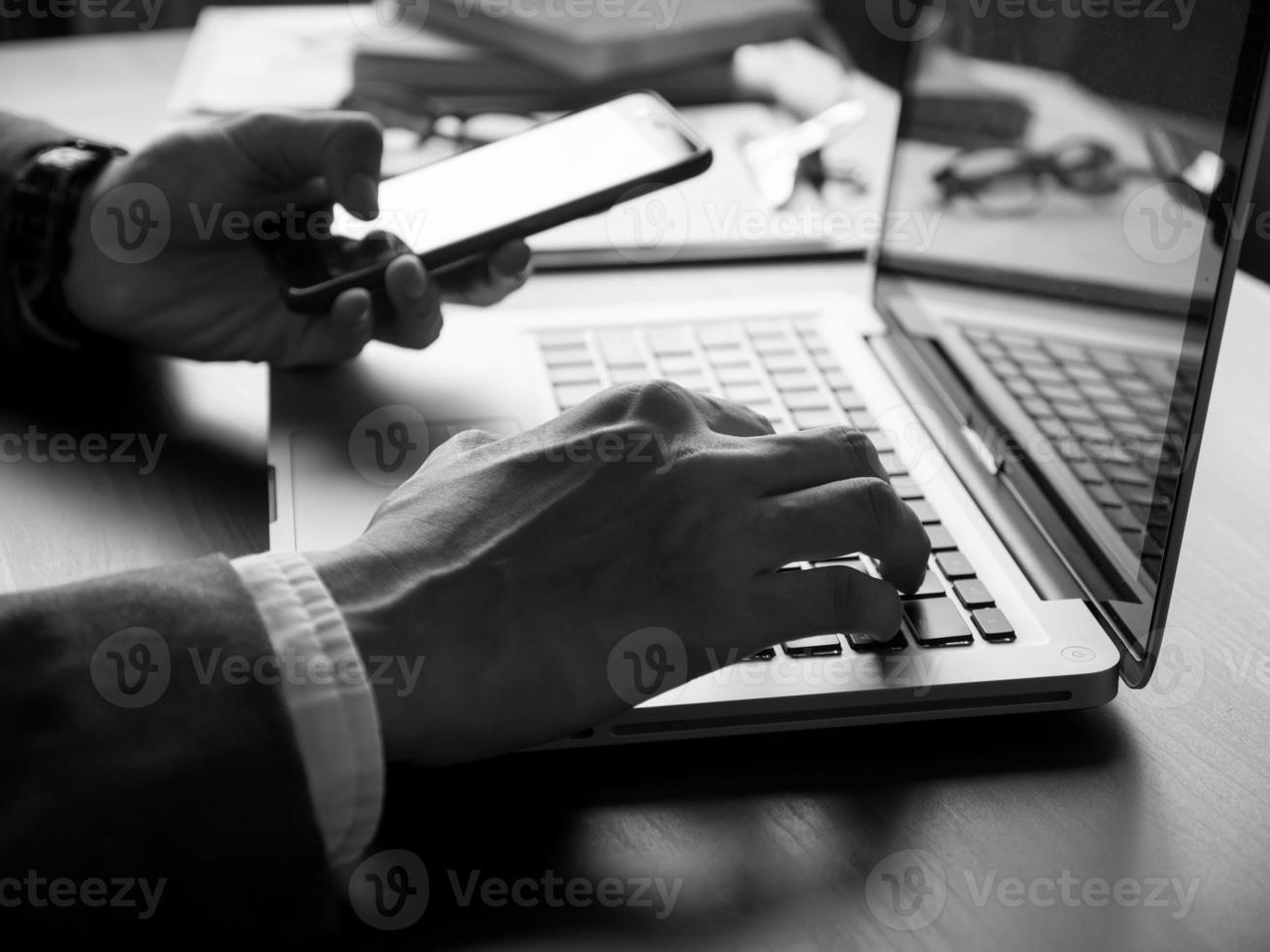 close-up do empresário usando laptop e smartphone na mesa do escritório. tom preto e branco foto