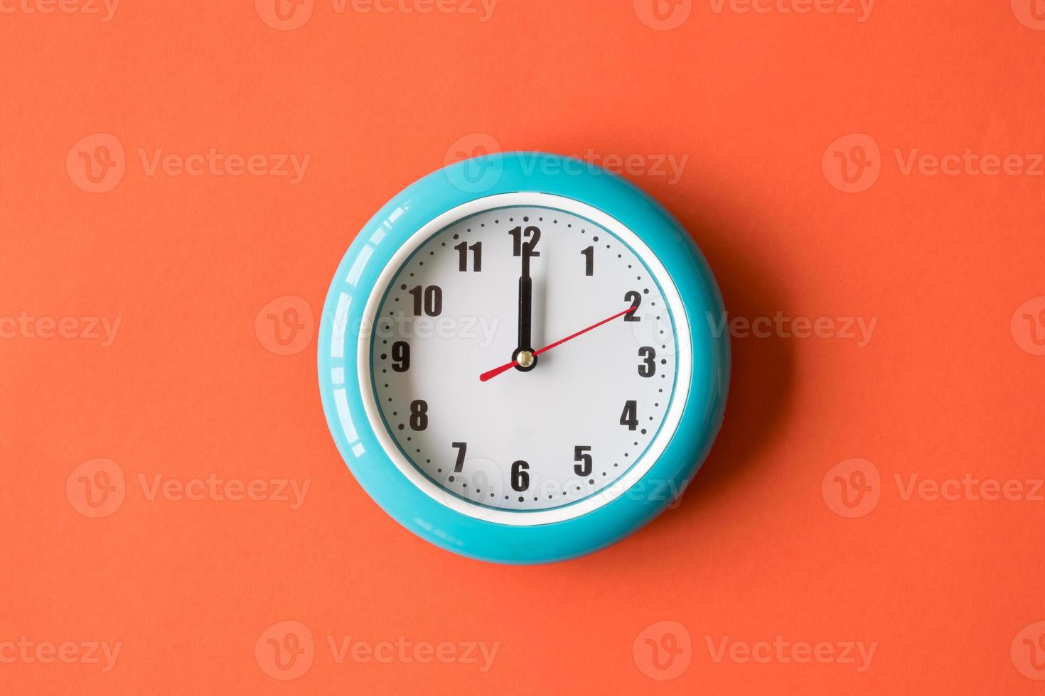 relógio de parede azul sobre fundo laranja, doze horas foto
