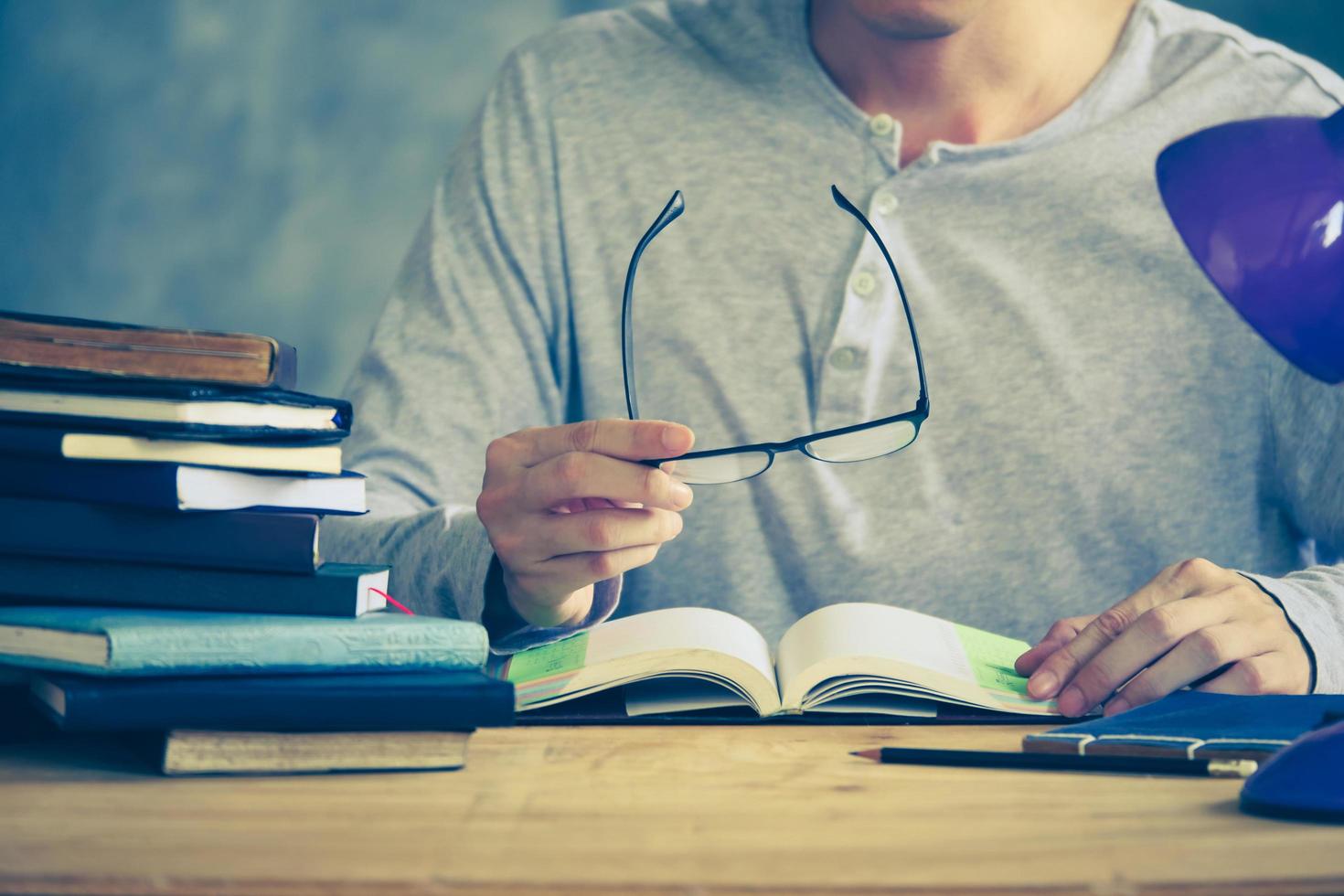 close-up de um homem segurando óculos e lendo um livro na mesa de madeira. tom vintage foto