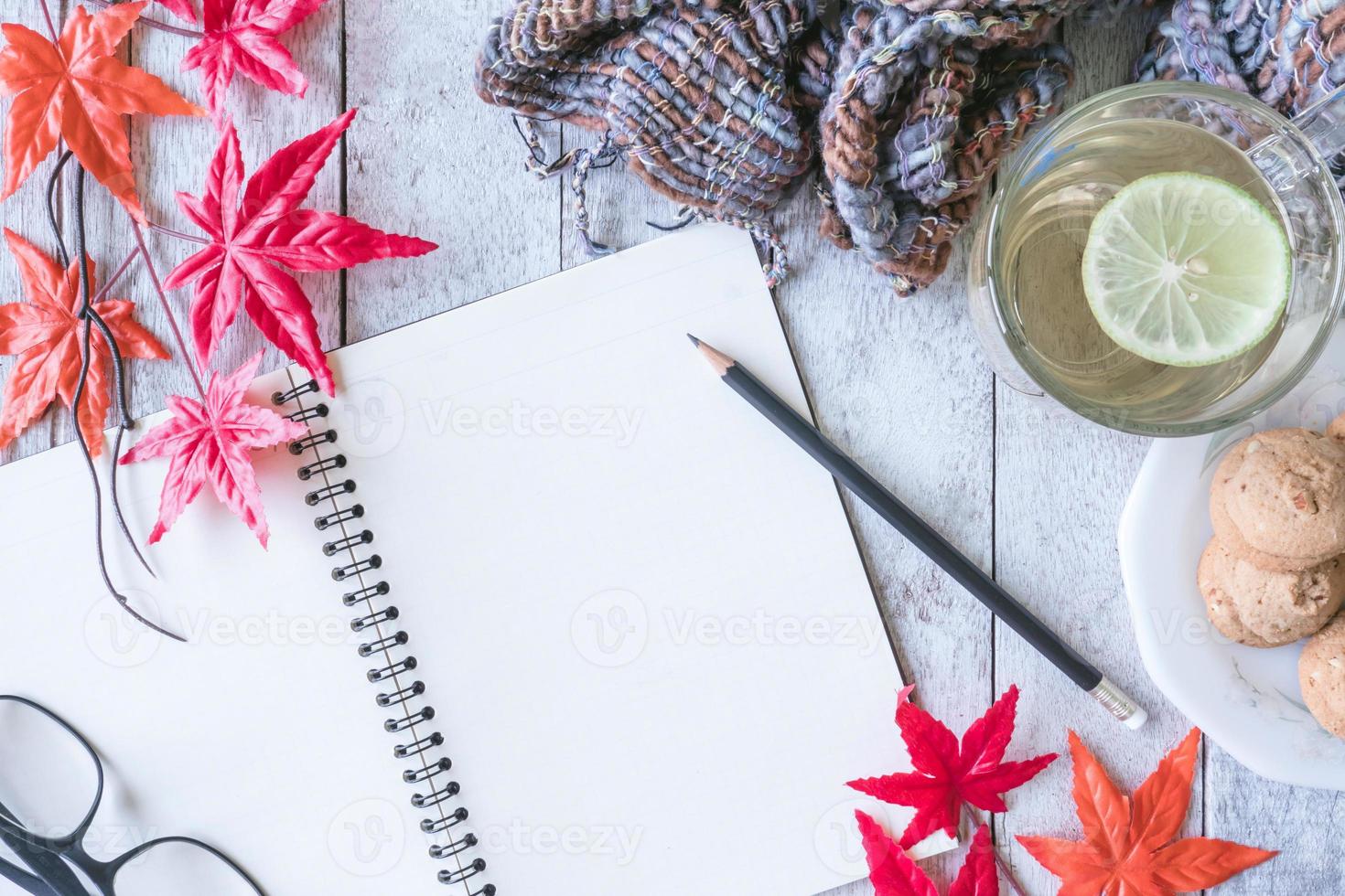 xícara de chá com limão, biscoito, cachecol, caderno, óculos, lápis e maple folhas na mesa de madeira. foto