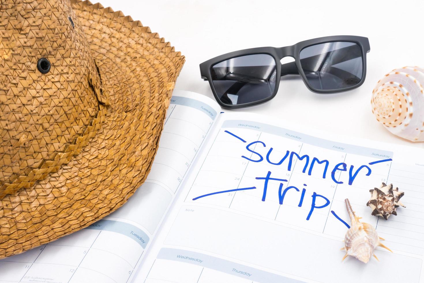 chapéu com óculos de sol, calendário e conchas em fundo branco, conceito de férias de verão foto