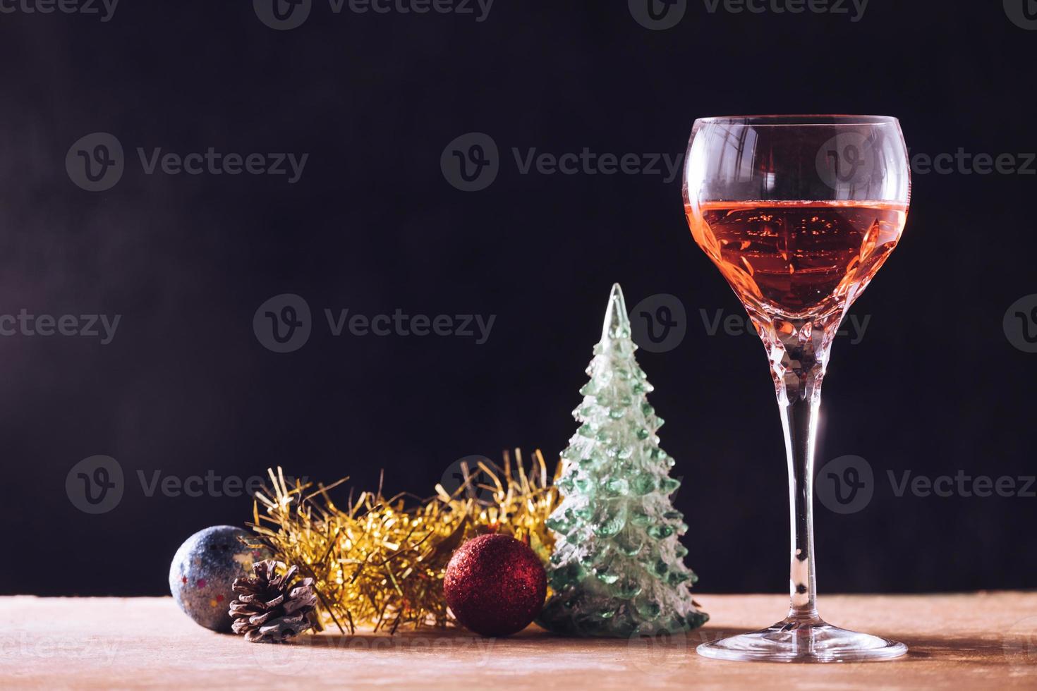 copo de vinho com enfeites de natal na mesa de madeira, fundo preto, espaço livre para texto foto