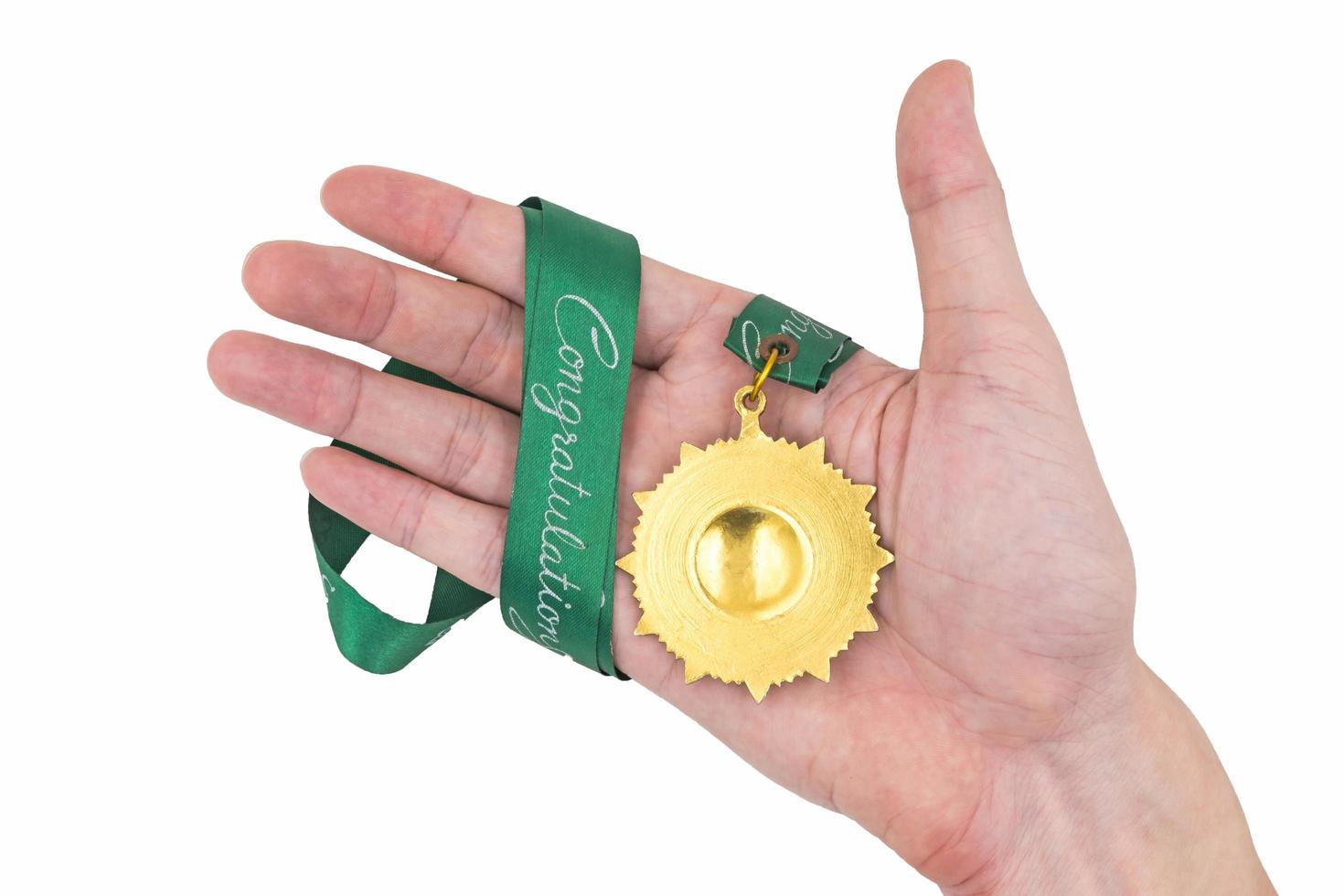 mão segurando a medalha de ouro com fita verde sobre fundo branco foto