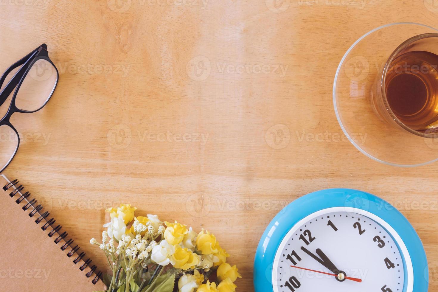 vista superior da xícara de chá com relógio, flor, notebook e óculos na mesa de madeira. espaço livre para texto foto